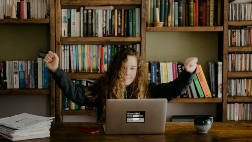 Une femme est assise à un bureau avec un ordinateur portable devant une bibliothèque.