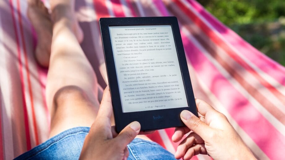 Une personne allongée sur un hamac lit un livre électronique sur une tablette.