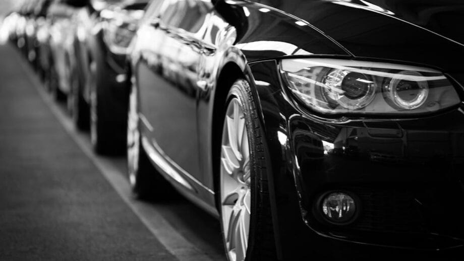Une photo en noir et blanc montrant une rangée de voitures garées en file, mettant l'accent sur les phares et les rétroviseurs brillants et détaillés de la voiture la plus en avant.