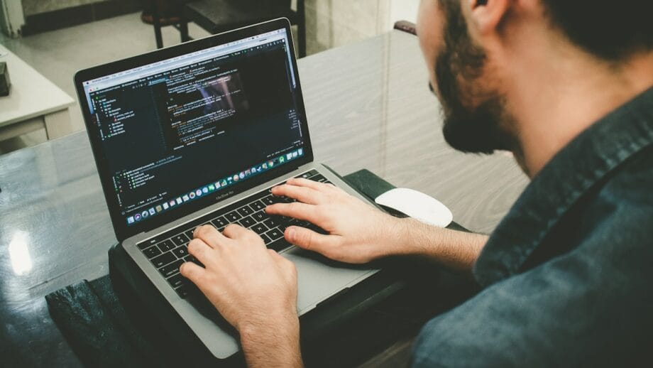 Homme travaillant sur un ordinateur portable avec du code à l’écran.