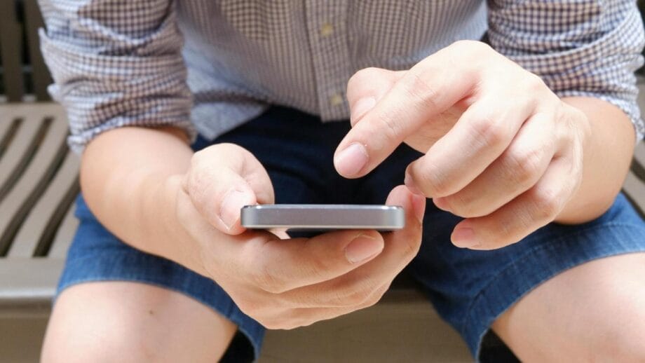 Une personne assise sur un banc en bois utilise un smartphone à deux mains.
