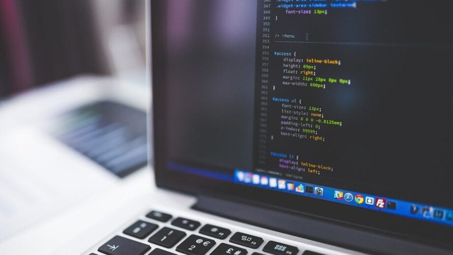 Un ordinateur portable affichant un éditeur de code avec du code HTML et CSS à l'écran. Le clavier et une partie d’un autre ordinateur portable flou sont visibles en arrière-plan.