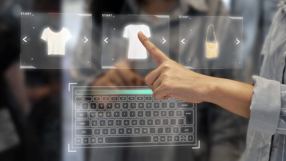 Une personne interagit avec une interface d'achat virtuelle à l'aide d'un écran tactile, en sélectionnant entre les images d'une chemise et un sac, avec un clavier holographique visible en dessous.
