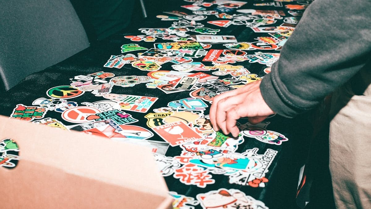 Atteindre la main pour les autocollants colorés répartis sur une nappe noire, avec une boîte en carton partiellement visible.