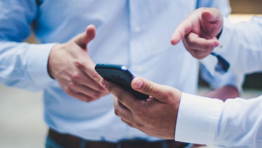 Une personne dans une chemise bleu clair tient un smartphone avec une main tout en faisant un geste avec l'autre main.