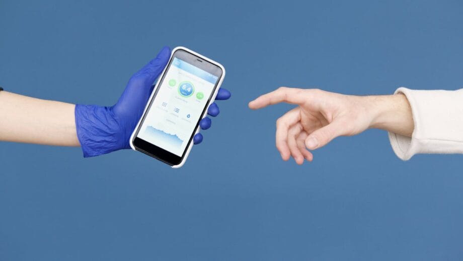 Une main gantée tient un smartphone affichant une application de santé car une main non gantée le atteint, sur fond bleu.