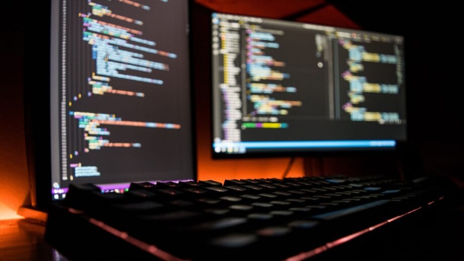 Un ordinateur avec deux moniteurs et un clavier montrant certains codes de programmation.