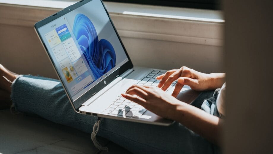 Personne utilisant un ordinateur portable doté d’une interface Windows 11, assise près d’une fenêtre à la lumière naturelle.