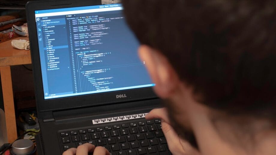Personne tapant du code sur un ordinateur portable Dell dans un espace de travail encombré. L'écran affiche l'interface de programmation.