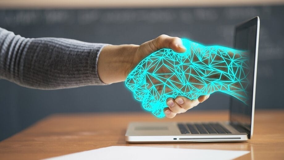 La main d'une personne s'étend vers un écran d'ordinateur portable avec un graphique représentant une poignée de main géométrique bleue, symbolisant la connectivité numérique ou les accords en ligne.