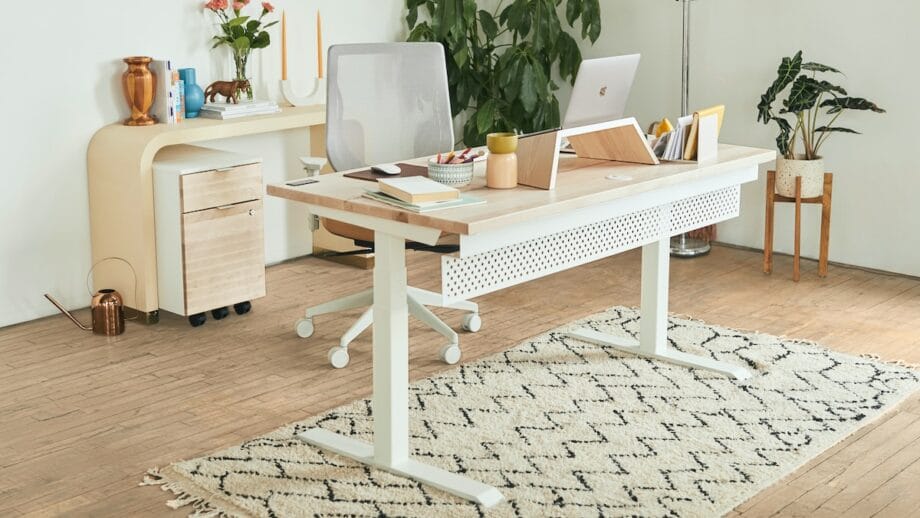 Un bureau blanc avec un ordinateur portable dessus et une plante dessus.
