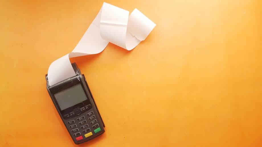 Un terminal de paiement par carte de crédit avec un long reçu se trouve sur une surface orange.
