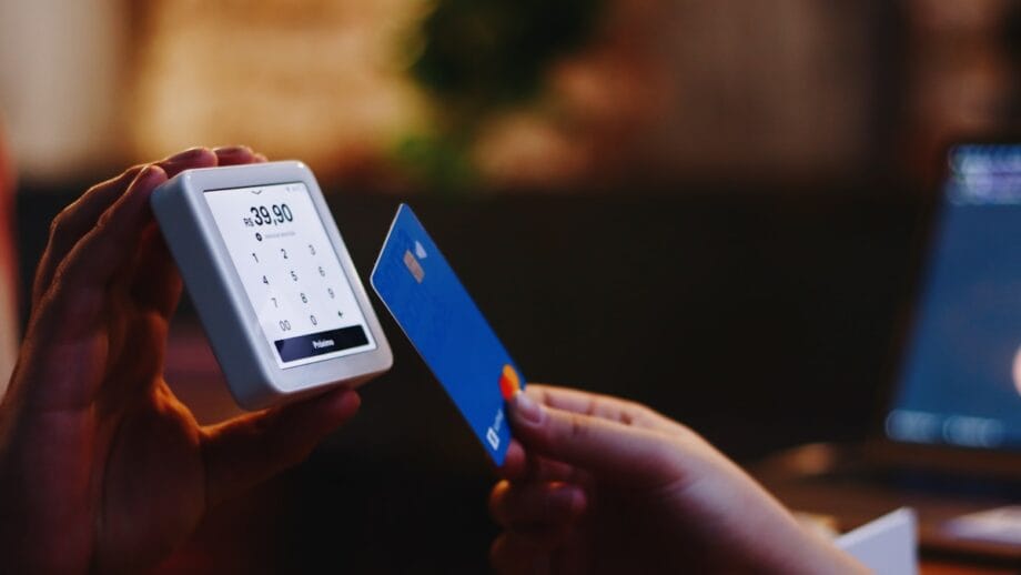 Une personne tient une carte de crédit bleue près d'un lecteur de carte affichant un montant de 39,90 pour un paiement sans contact.