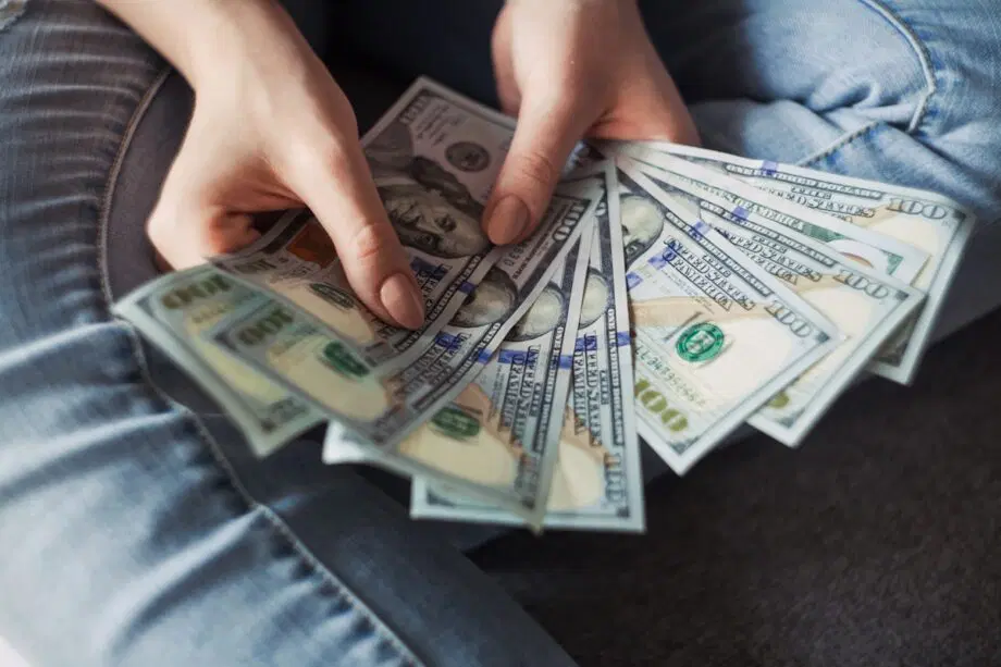 Personne tenant et déployant plusieurs billets de 100 dollars américains tout en étant assise, les jambes croisées.