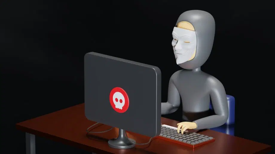 Illustration 3D d'un pirate informatique portant un sweat à capuche gris et un masque utilisant un ordinateur avec un symbole de crâne rouge sur le moniteur.