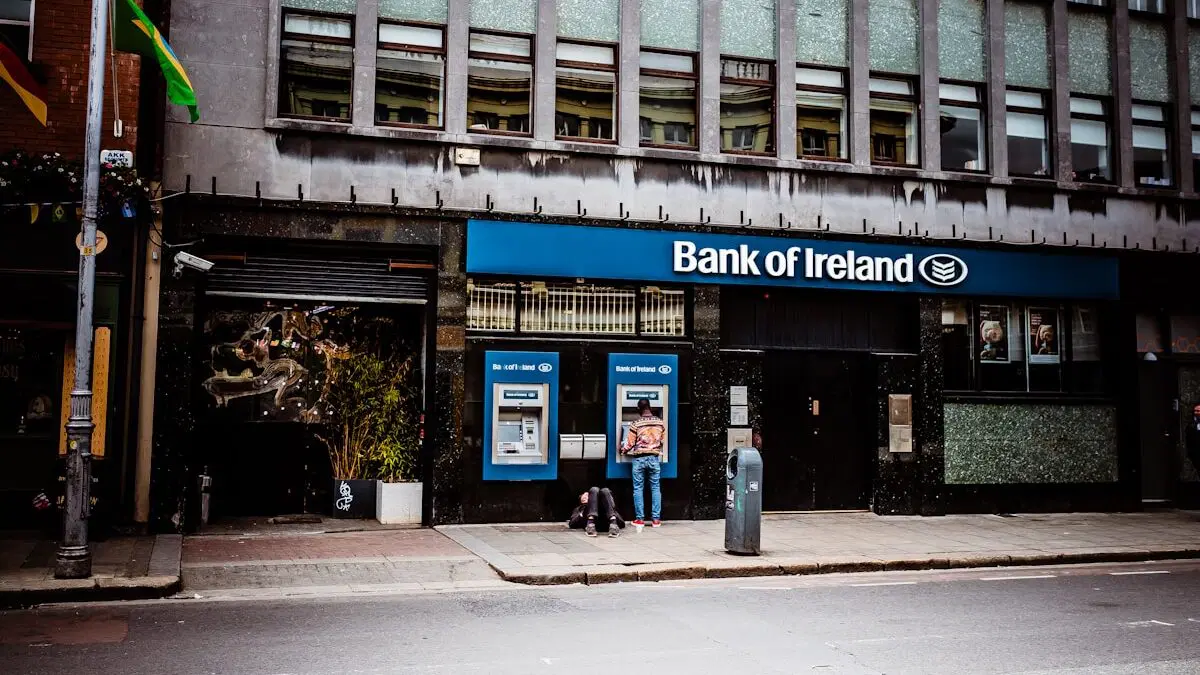 Personne utilisant un guichet automatique à l'extérieur d'une succursale de la Bank of Ireland dans une rue de la ville pendant la journée.