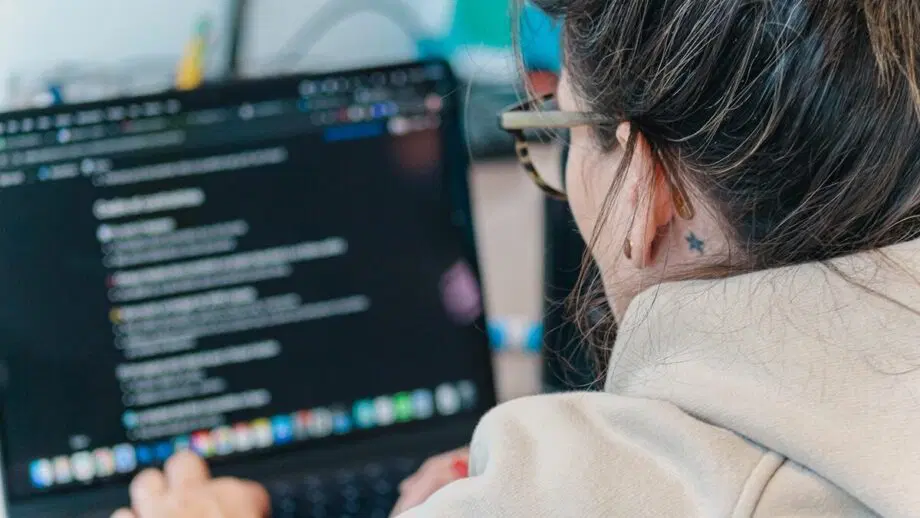 Une personne portant des lunettes travaille sur un ordinateur portable affichant des lignes de code sur l'écran.