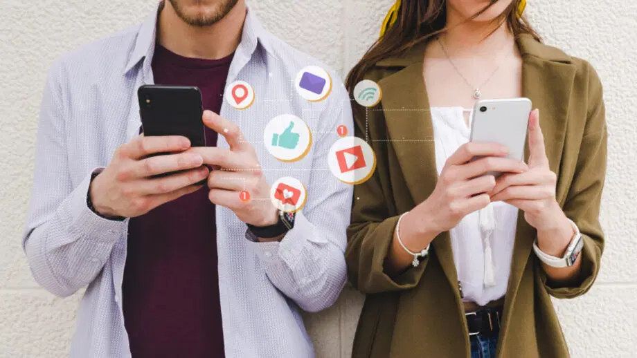 Deux personnes utilisent des smartphones avec des icônes de réseaux sociaux telles que des likes, des messages et des notifications illustrées entre elles.