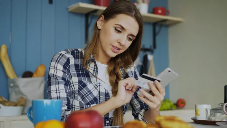 Femme utilisant une carte de crédit avec un smartphone à table