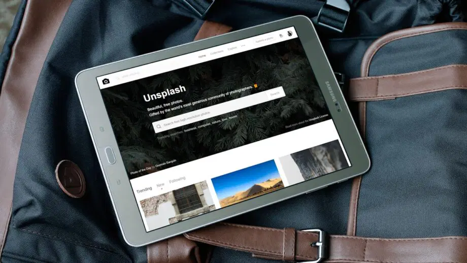 Une tablette affichant le site Web Unsplash repose sur un sac de voyage noir et marron.