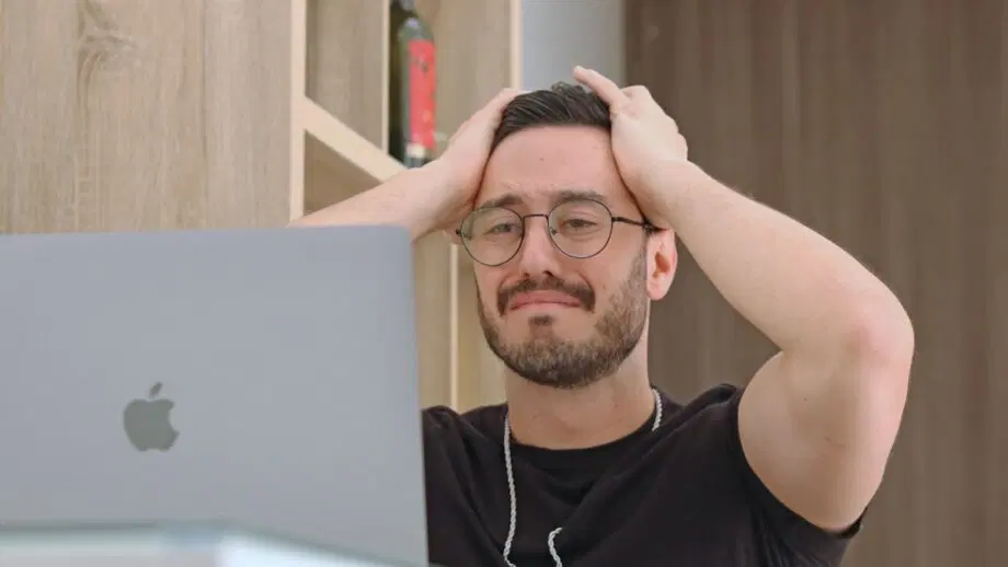 Un homme avec des lunettes semble frustré alors qu'il se tient la tête à deux mains devant un ordinateur portable.