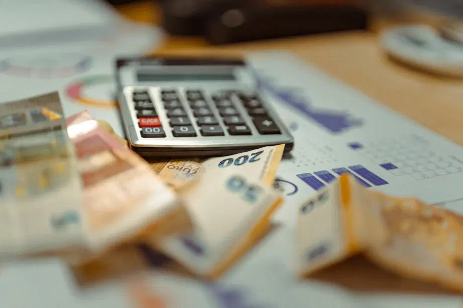 Une calculatrice et plusieurs billets en euros au-dessus des tableaux et documents financiers.