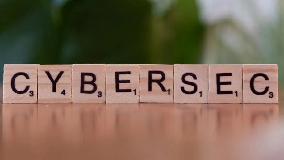 Sept lettres en bois épellent CYBERSEC sur une surface en bois avec un arrière-plan vert flou.