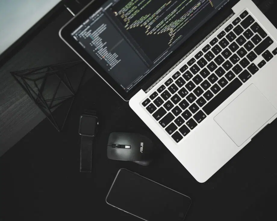 Ordinateur portable affichant le code à côté d'une montre intelligente, d'une souris sans fil et d'un téléphone sur un bureau noir.