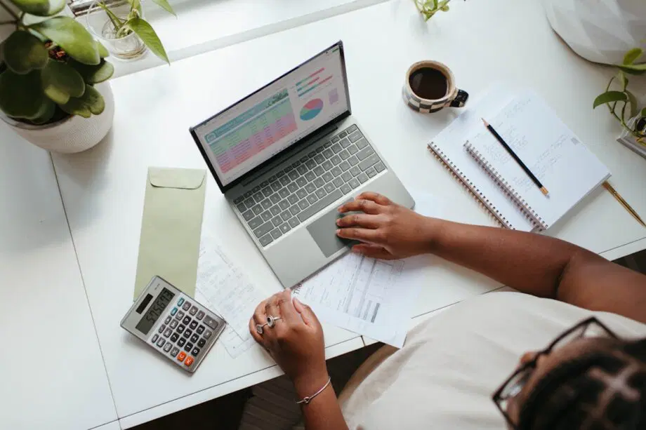Personne travaillant à un bureau avec un ordinateur portable affichant des graphiques, une calculatrice, des documents, un bloc-notes, un crayon et une tasse de café.
