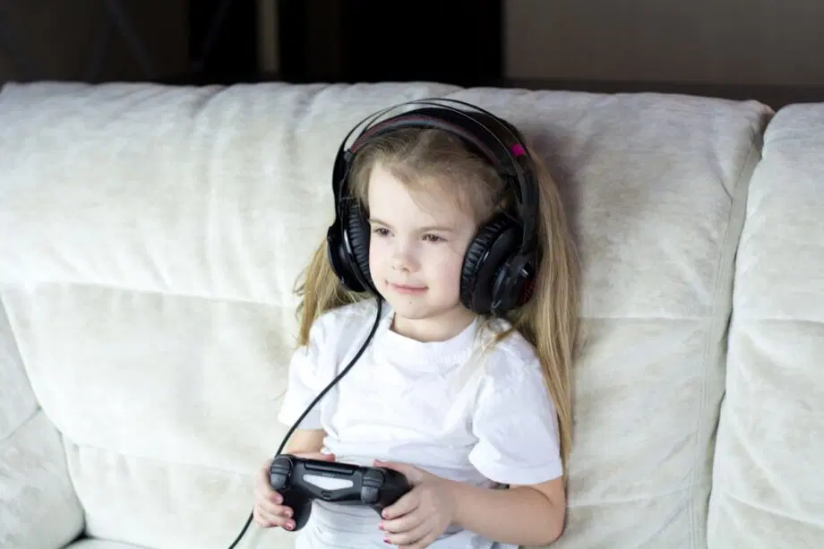 Une jeune fille portant des écouteurs est assise sur un canapé et tient une manette de jeu vidéo.