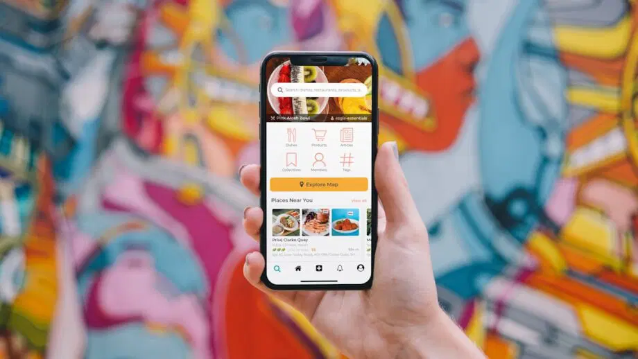 Une main tenant un smartphone affichant une application de livraison de nourriture, avec une fresque colorée en arrière-plan.
