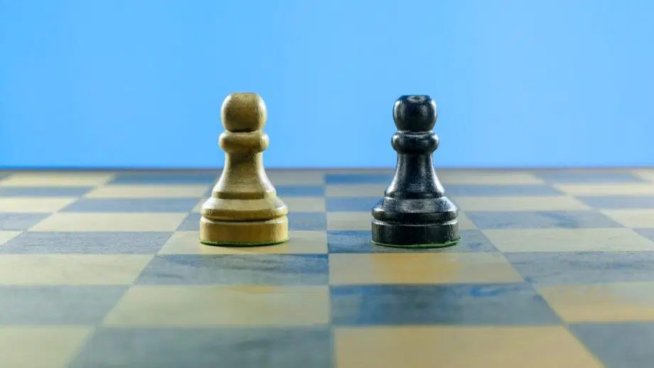 Deux pions d'échecs, un clair et un foncé, se tiennent côte à côte sur un échiquier à fond bleu.