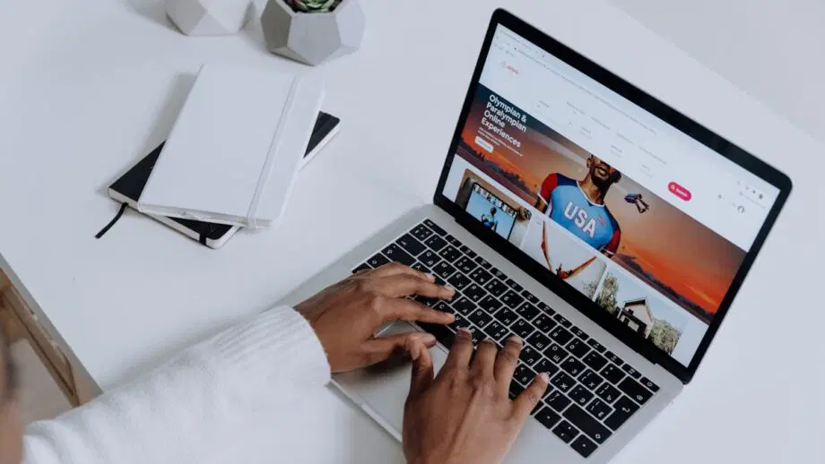 Personne tapant sur un ordinateur portable affichant un site Web, avec des cahiers et des plantes en pot sur un bureau blanc.